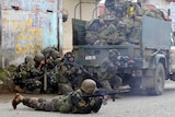 Philippines government troops crouch on the ground and prepare to fire their weapons.