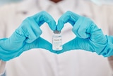 Gloved hands make a heart and hold a vial of COVID vaccine