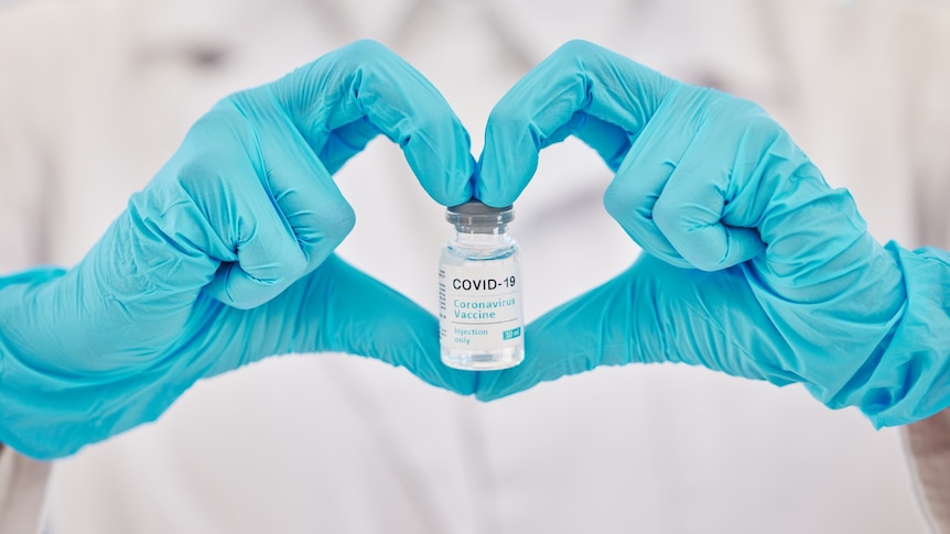 Gloved hands make a heart and hold a vial of COVID vaccine