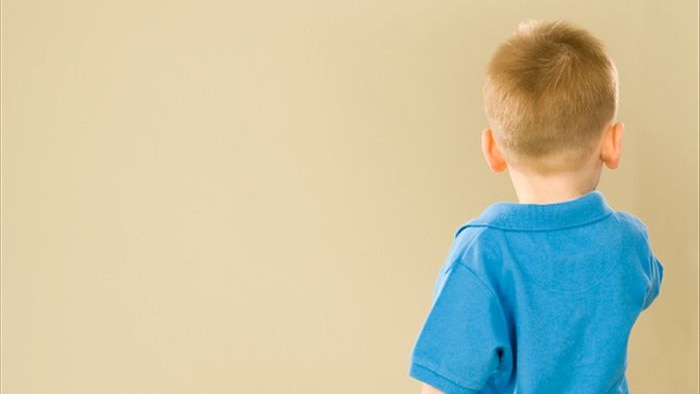 A small child standing with his back to the camera looking towards a wall.
