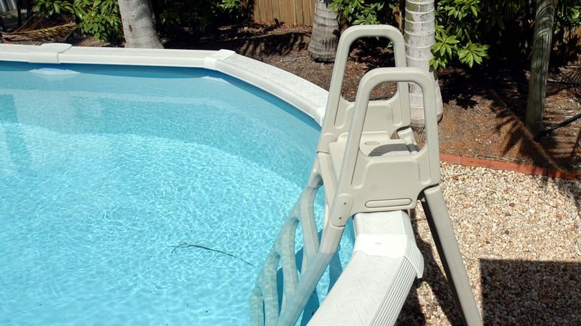 An above ground swimming pool sits in a back yard