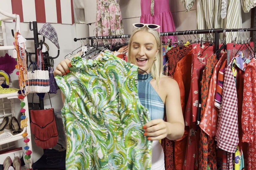 Blonde woman smiles as she inspects a vintage clothing item