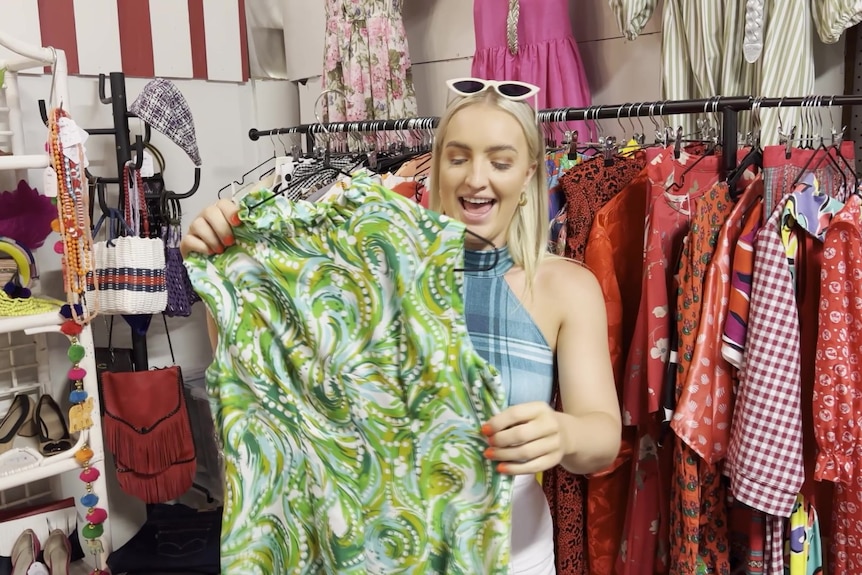 A blonde woman smiles while checking an old piece of clothing