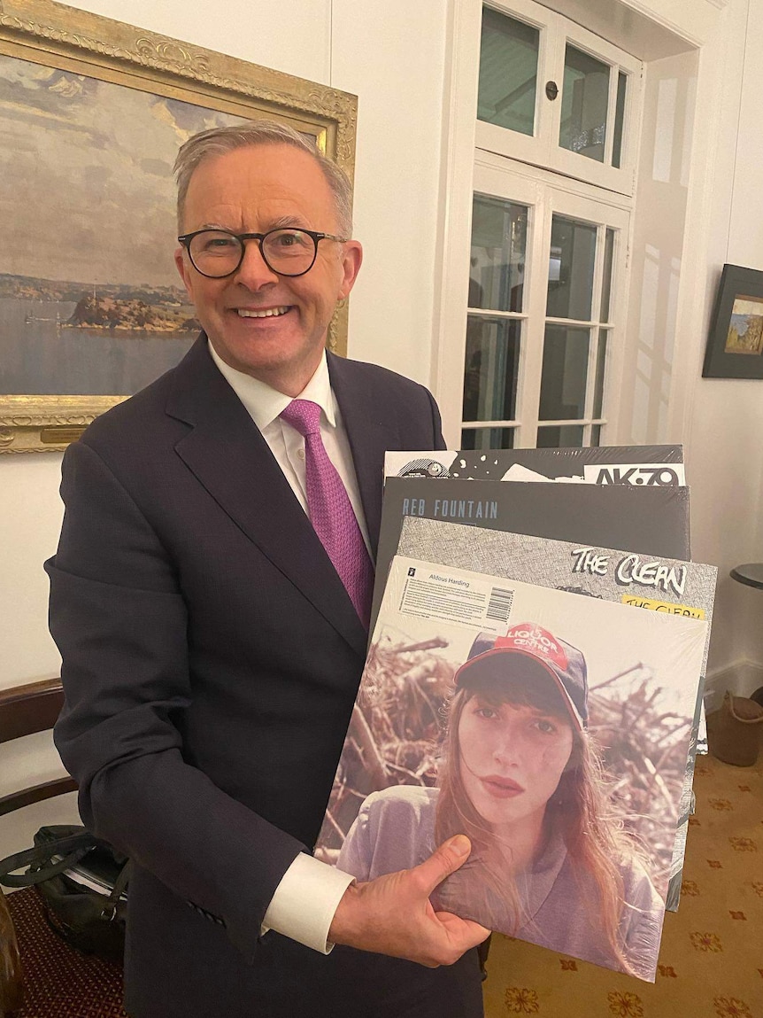 Prime Minister Anthony Albanese smiles and holds four vinyl records by New Zealand artists Aldous Harding, The Clean and more