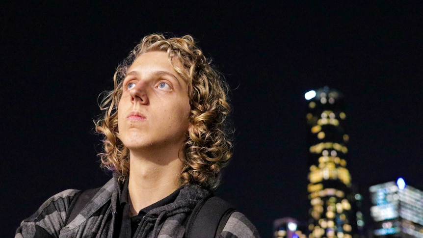 young person with curly hair and nighttime Brisbane city skyline in background
