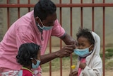 A man wearing a face mask puts face masks on two small children.