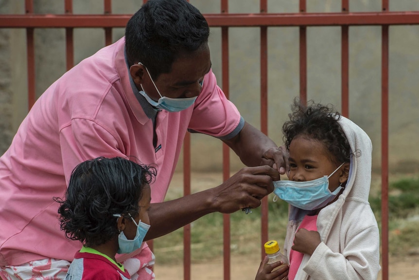 A man wearing a face mask puts face masks on two small children.