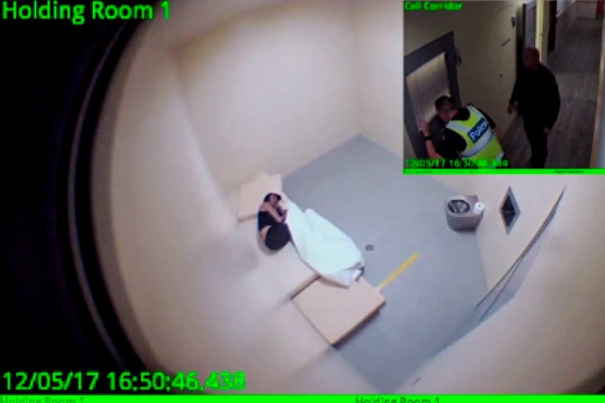 CCTV still of woman in cell lying on bed with policeman peering through door