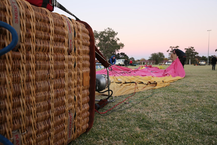 A hot air balloon basket sits near a deflated balloon on a sports field.