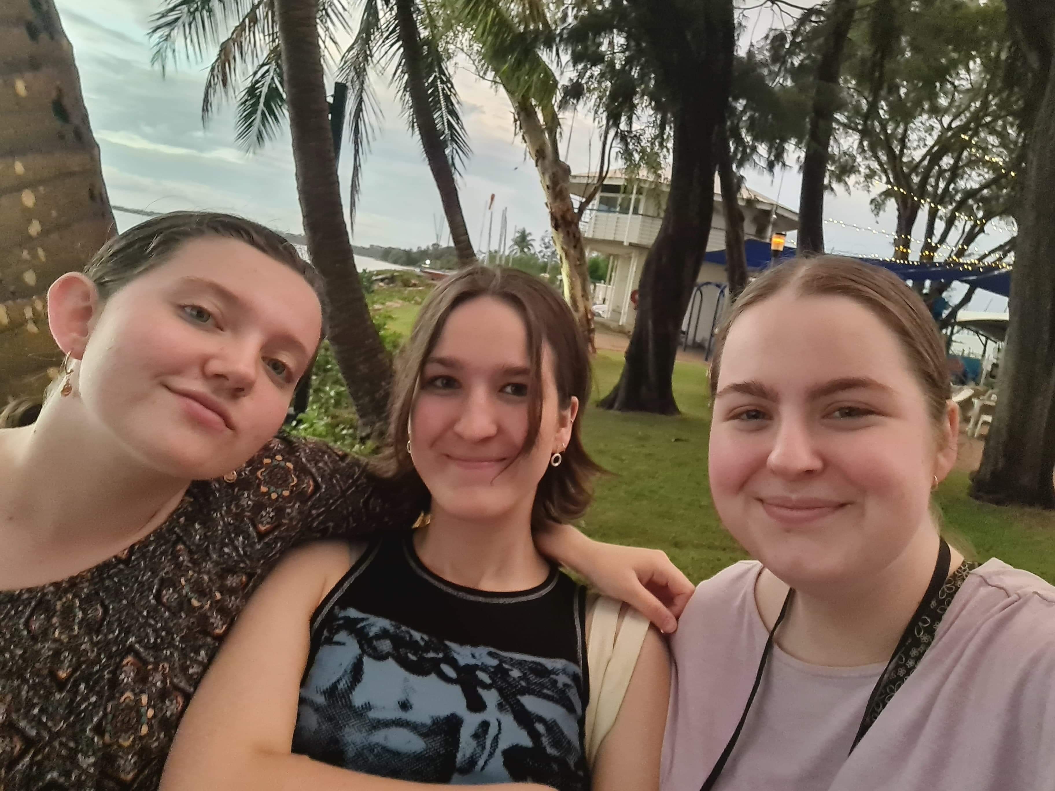 Three teenage girls stand in front of Darwin's coastline. 