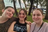 Three teenage girls stand in front of Darwin's coastline.