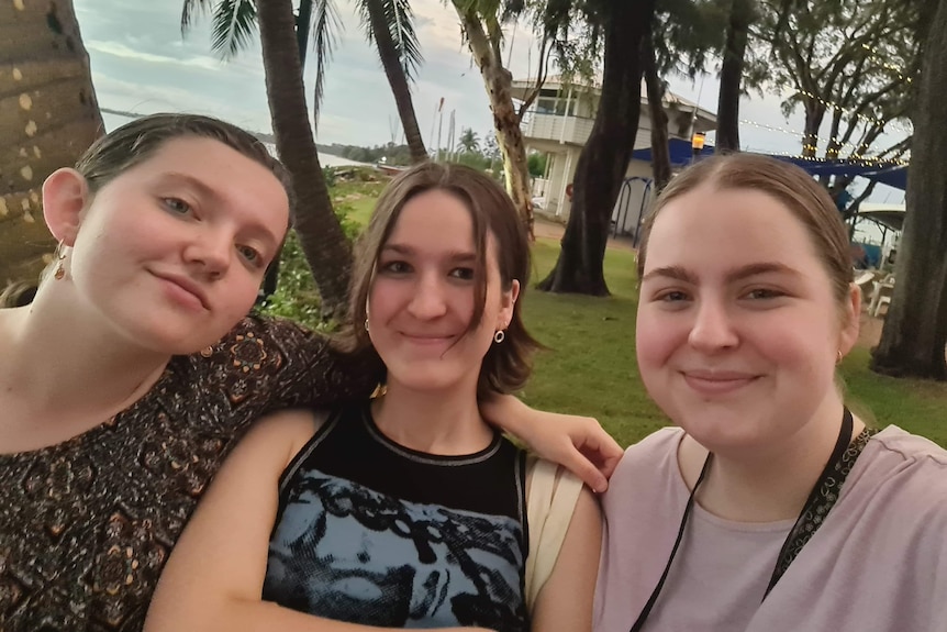 Three teenage girls stand in front of Darwin's coastline. 