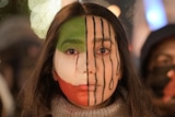 Woman with facepaint showing part Iranian flag, part hanging nooses