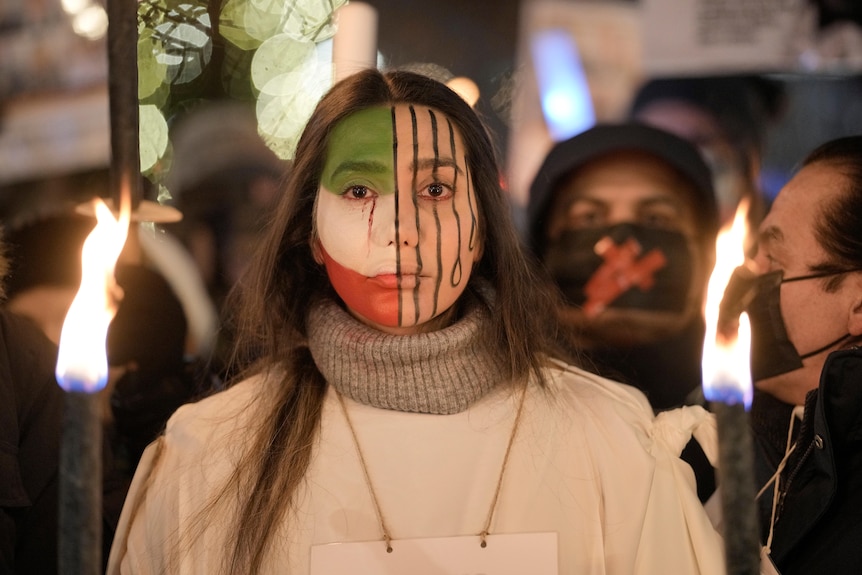 A woman with her face painted half in Iran flag colours and half in black lines showing prison bars and noose