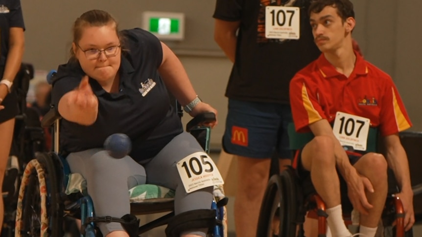 Boccia player Jessi Hooper is sitting in her wheelchair, and throws a boccia ball underarm.