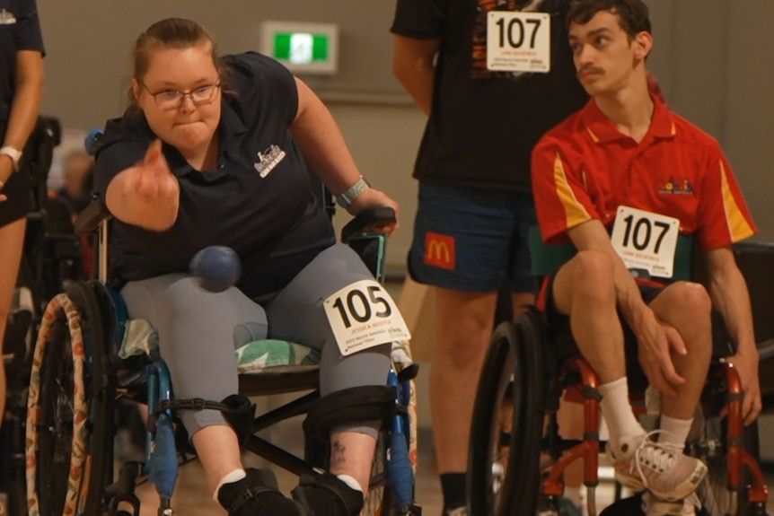 Boccia player Jessi Hooper is sitting in her wheelchair, and throws a boccia ball underarm.