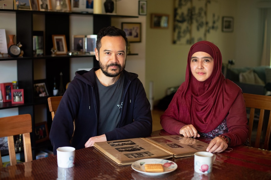 A man in a navy hoodie and a woman in a burgundy hijab sitting at a dining table with a photo album