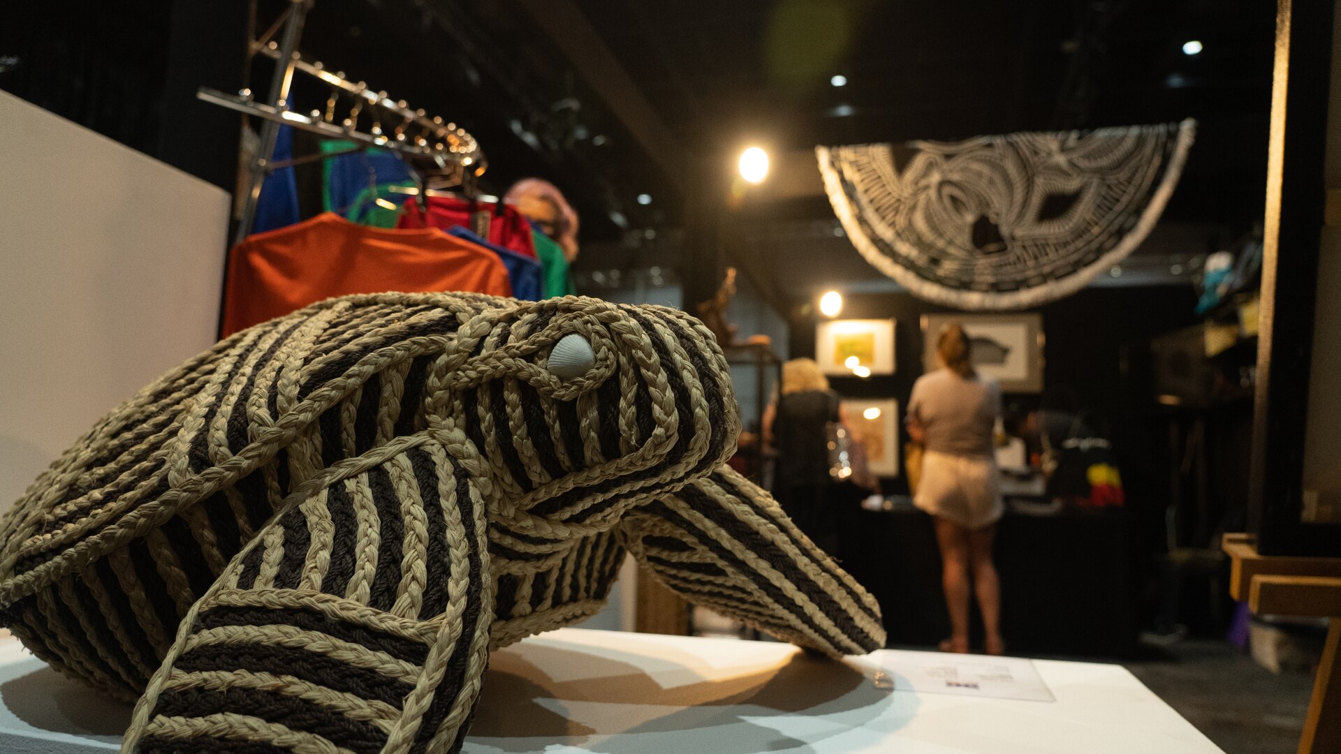 A woven turtle sculpture on a table, as an art fair goes on in the background.
