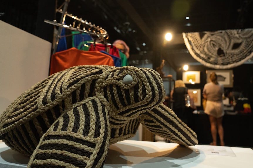 A woven turtle sculpture on a table, as an art fair goes on in the background.