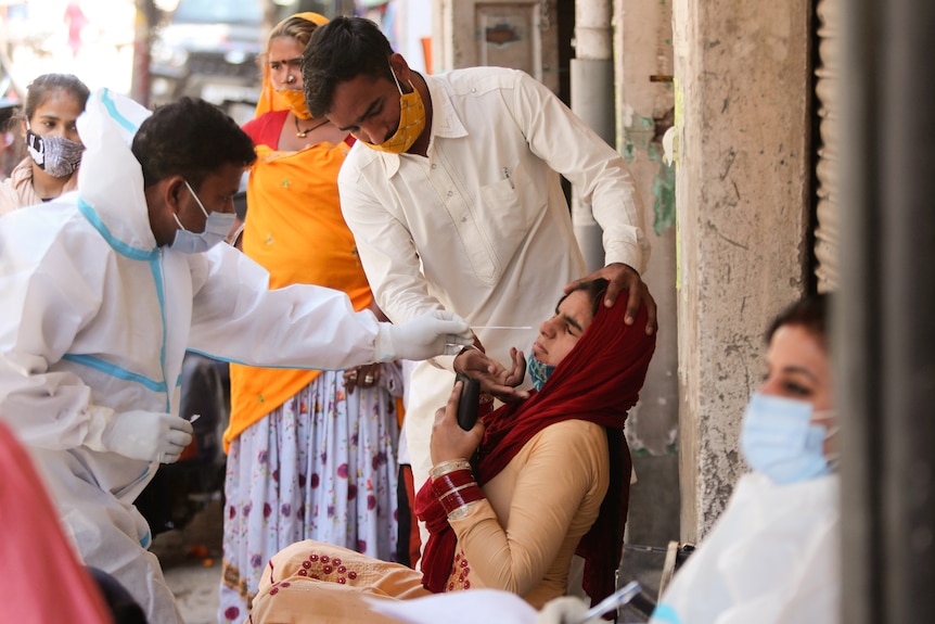 A woman leans away as a man in white scrubs tries to take a nasal sample.