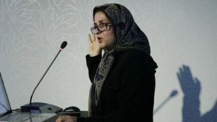 Meimanat Hosseini Chavoshi speaks at a lectern, with her shadow visible on the wall behind.