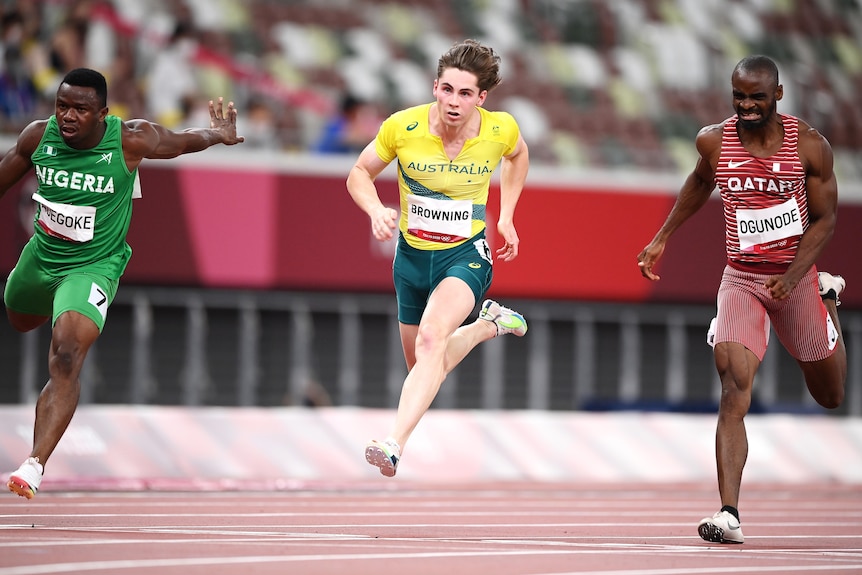 Three male sprinters competing in the 100 metres semi-finals at the Tokyo Olympics.