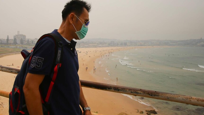 A man wears a mask while walking around Bondi Beach.