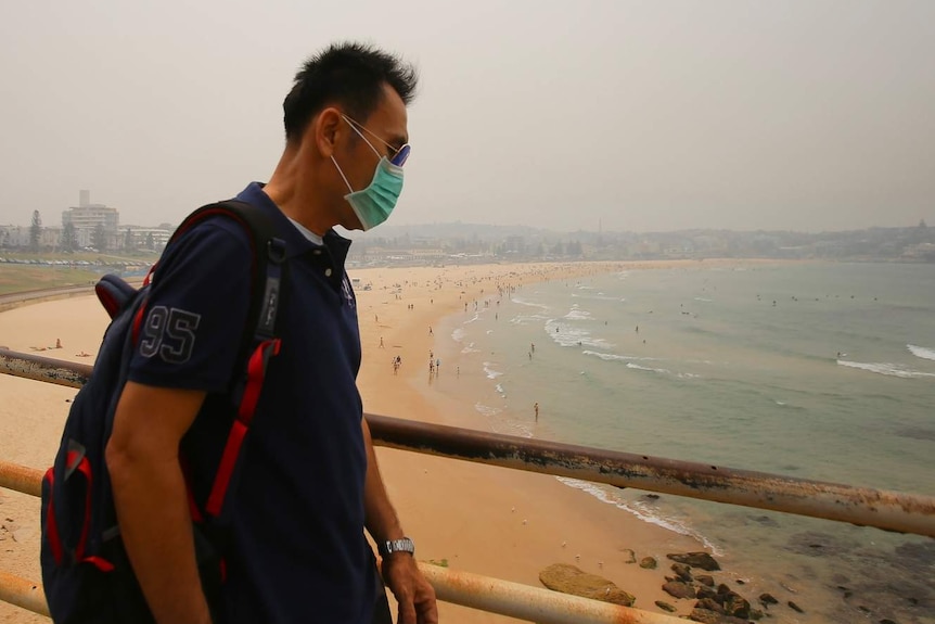 A man wears a mask while walking around Bondi Beach.