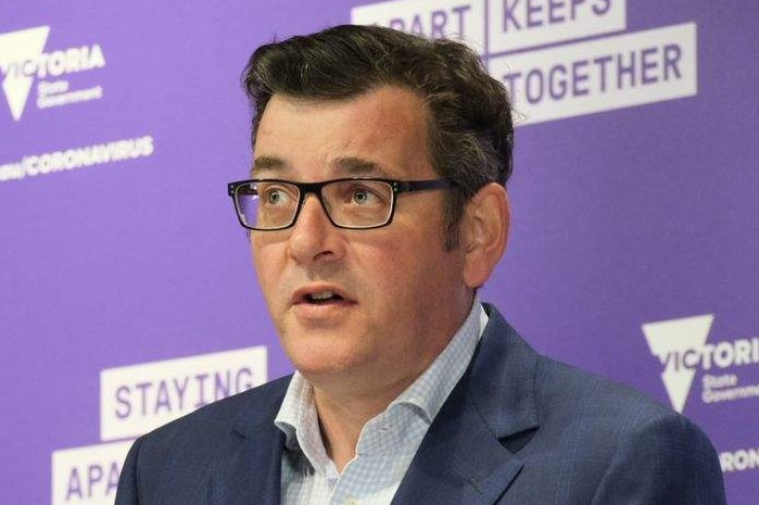 Daniel Andrews, dressed in a shirt and jacket, stands at a lectern with microphones in front of a purple background.