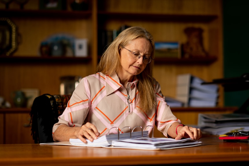 NT Acting Coroner, Judge Elisabeth Armitage, sitting at a desk inside an office and reading papers in a file. 