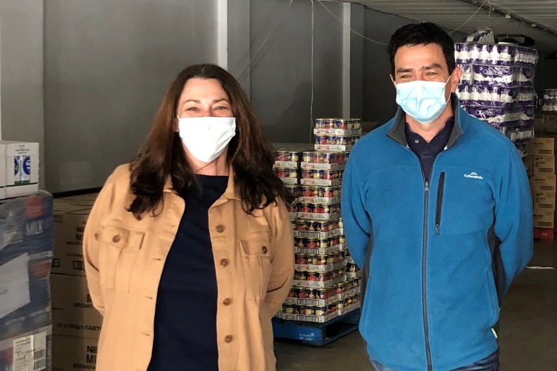 A woman and man wearing masks standing in a warehouse with boxes behind them