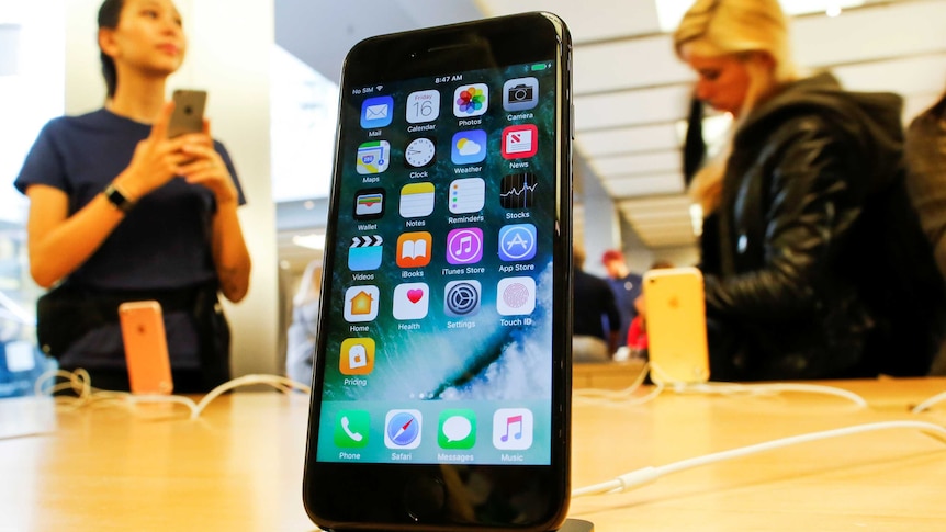 A jet black iPhone 7 sits in a dock on a table at an Apple Store.