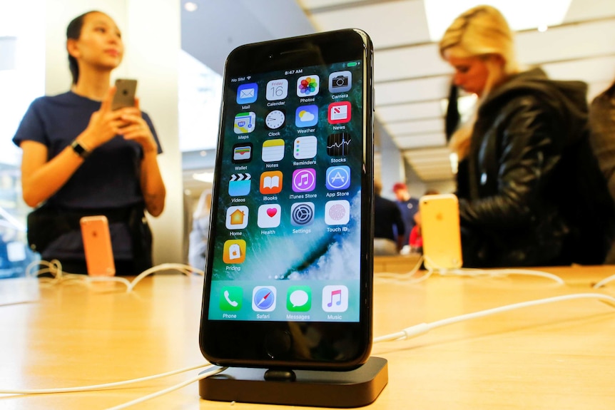 A jet black iPhone 7 sits in a dock on a table at an Apple Store.