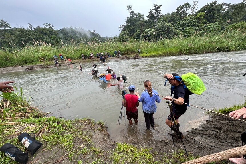 A group of people crossing a river in a jungle. 