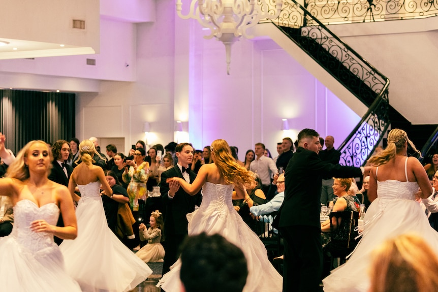 Dancers wearing formal attire spin across a dance floor with a staircase in the background.