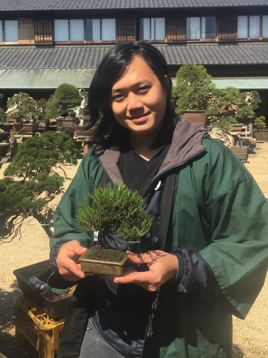 Bonsai apprentice Austen Kosasih holding a small tree.
