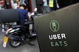 A close-up of UberEATS delivery drivers on scooters parked in front of a restaurant.