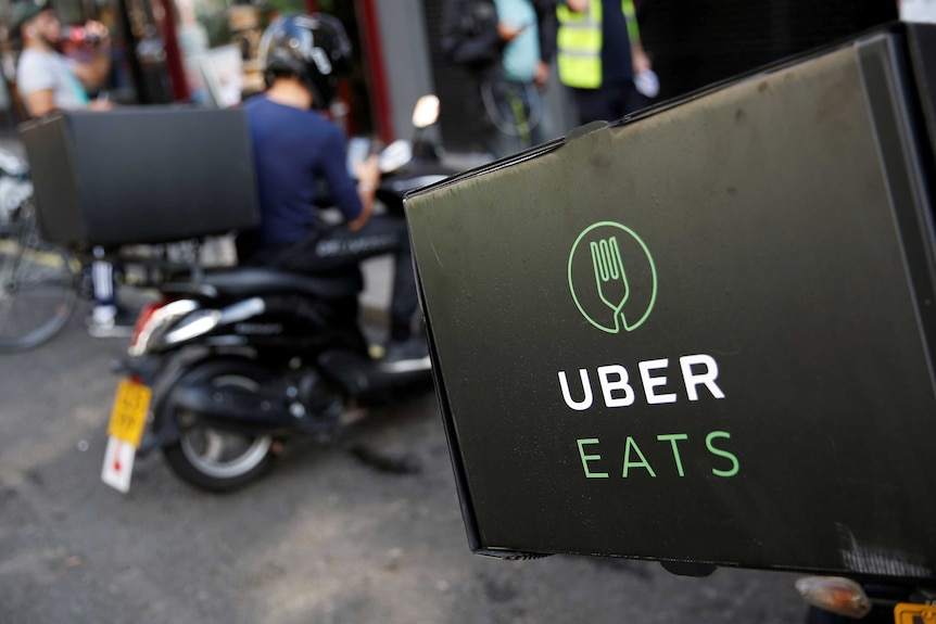 A close-up of Uber Eats delivery drivers on scooters parked in front of a restaurant.