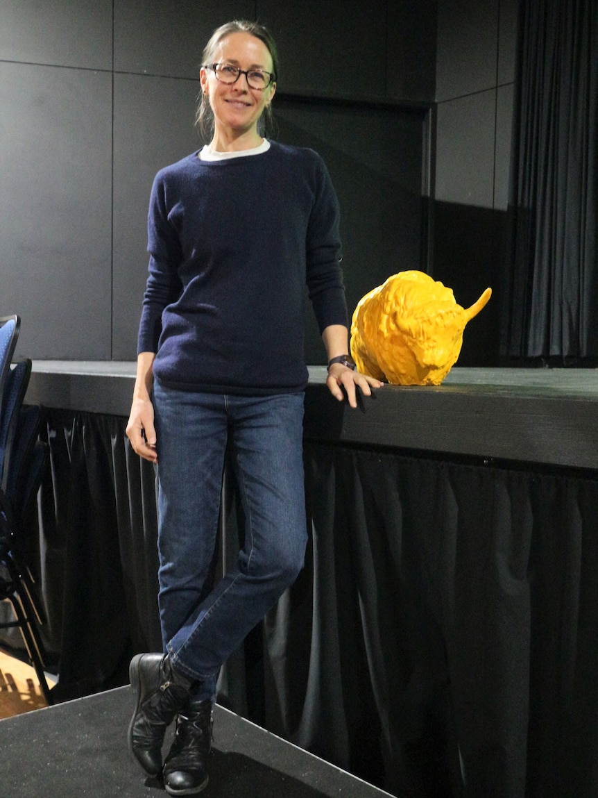 A young woman standing next to a small yellow sculpture of a yak