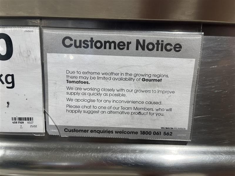 A sign on a supermarket shelf saying gourmet tomatoes are unavailable due to extreme weather in growing regions.