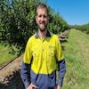 A man with wearing a high visibility shirt stands in an orchard.