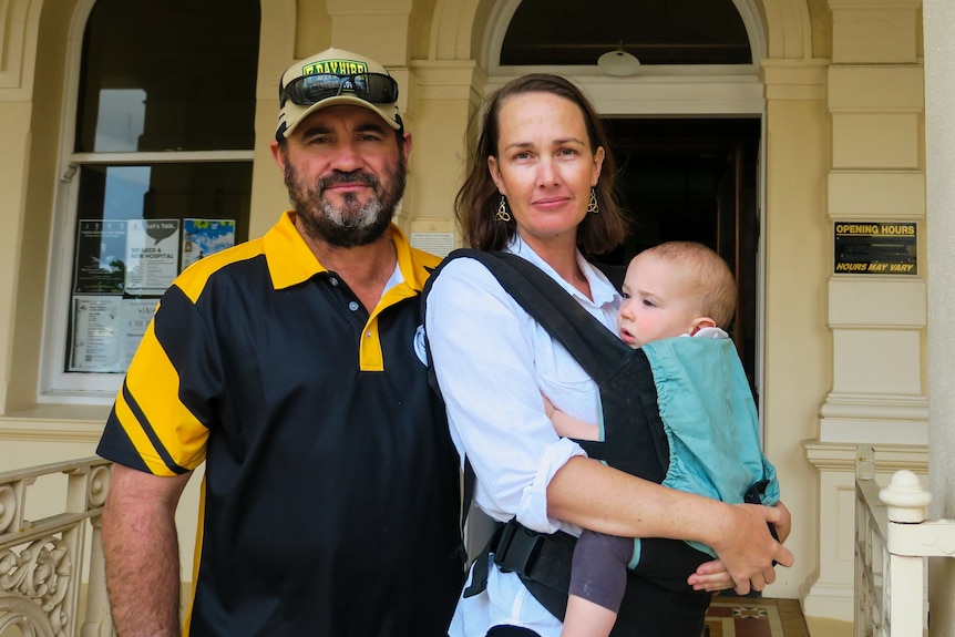 A woman and her husban look seriously at the camera while holding a young child