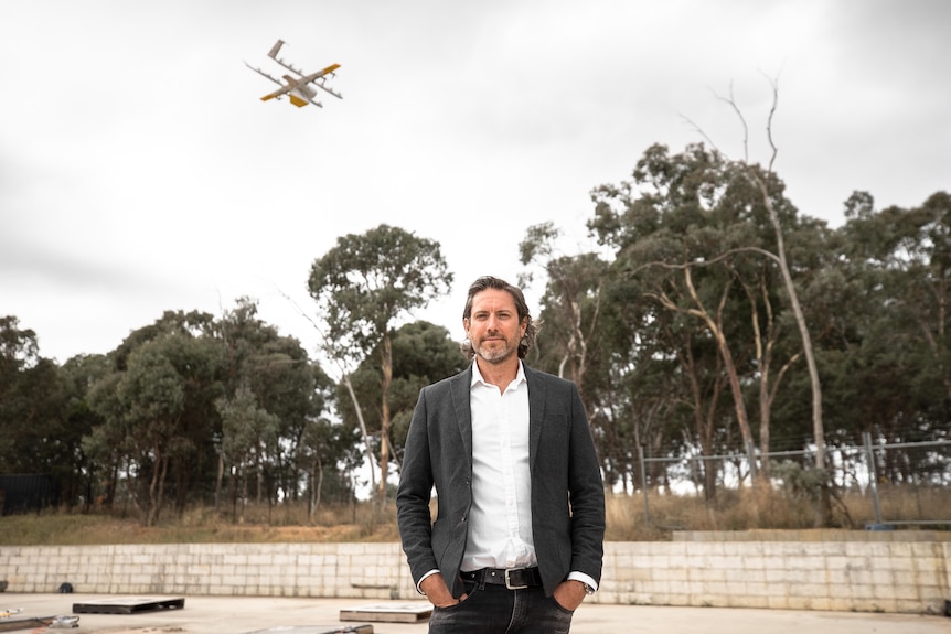 a man in a suit with a drone flying above him in a paddock