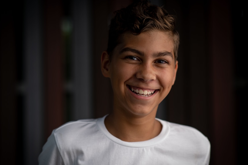 a young boy wearing a white shirt smiles at the camera. He has a big grin on his face.