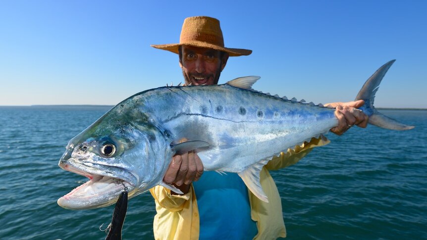 Man holds very large queenfish and looks very happy about it