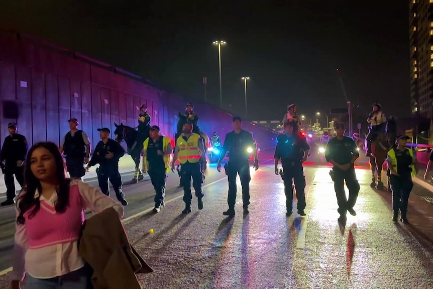 A line of police walks towards the camera on a road