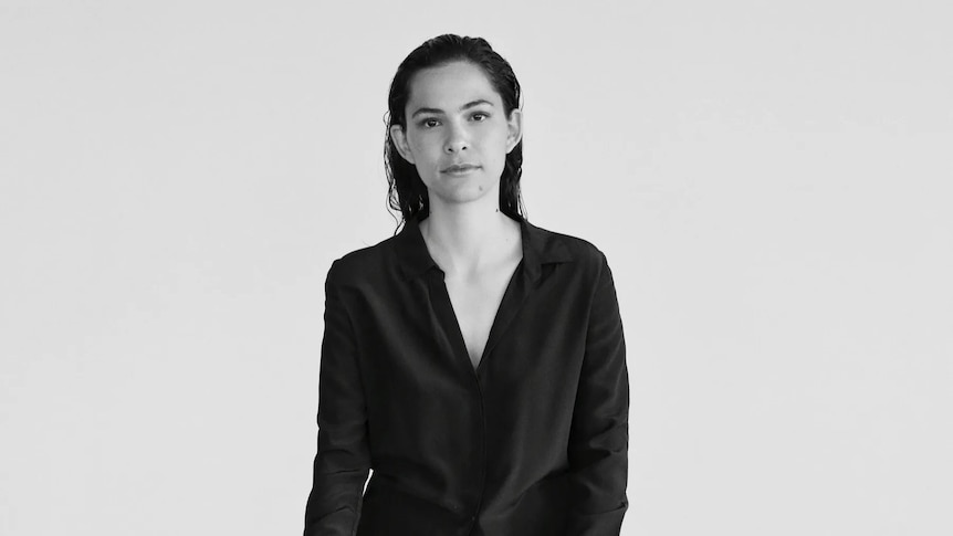 A monochrome photo of Dida Pelled in a black dress standing in front of a white wall