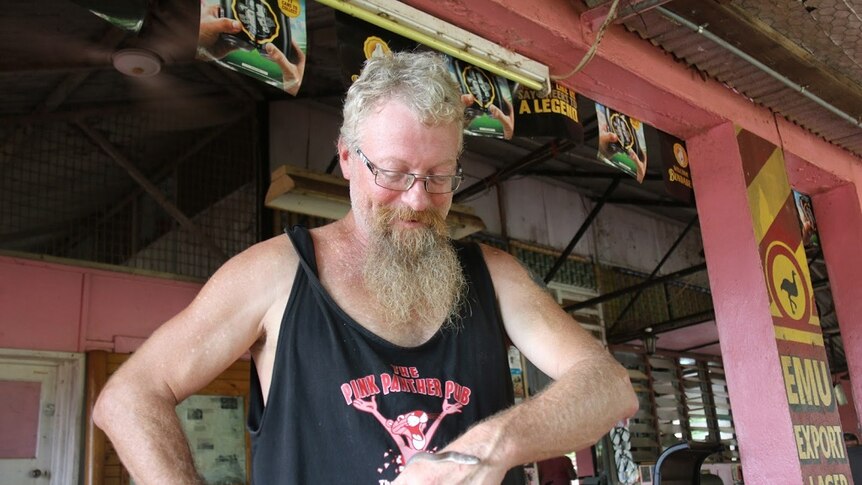 A man smiles as he looks down at a small snake coiling around his left hand.