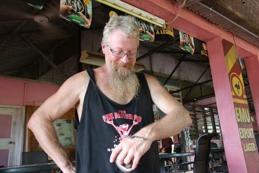 A man smiles as he looks down at a small snake coiling around his left hand.