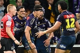 Four Melbourne Storm NRL players celebrate a try as the referee looks on.